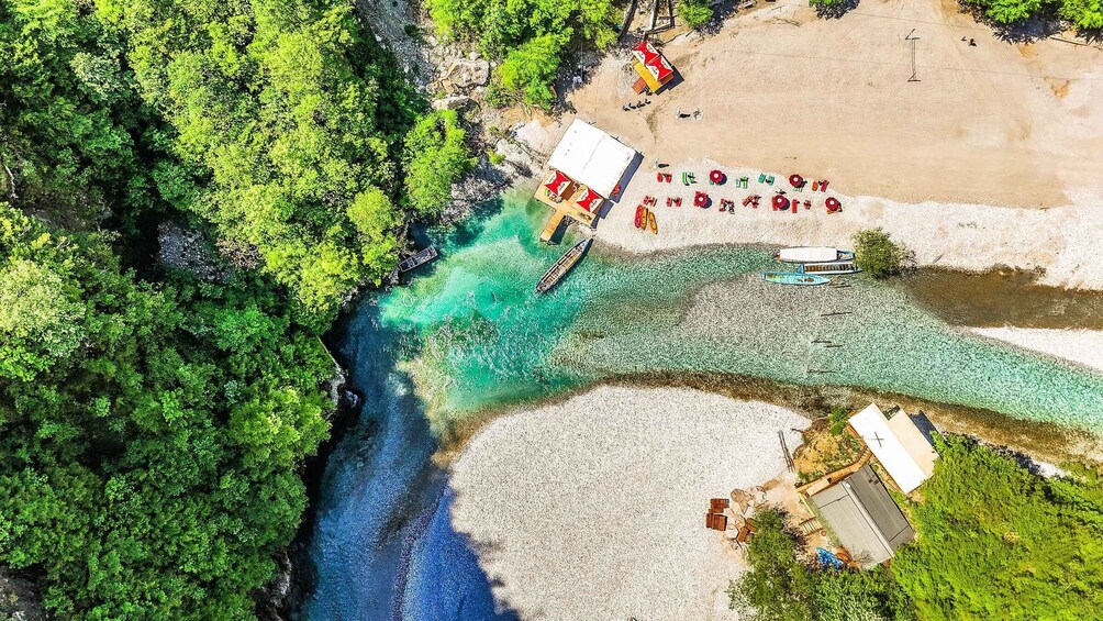 A river flowing through a forest into a beach area with a small dock and boats. 4