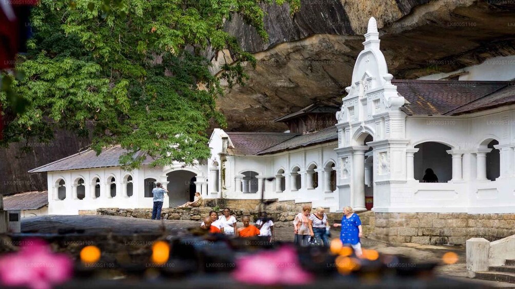 A white temple with a large central spire, surrounded by a stone wall and lush greenery. 1