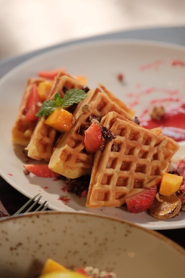 A plate of waffles with fruit and syrup. 2