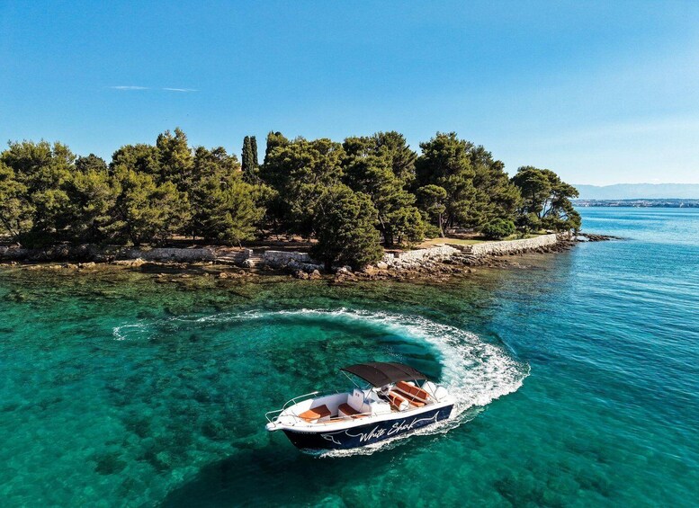 A boat named 'White Shark' moving through clear turquoise waters near a rocky coastline with dense green trees. 3