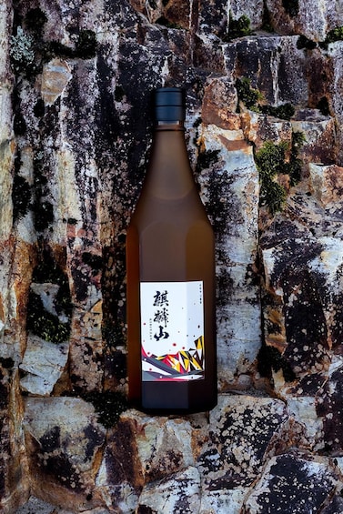 A bottle of sake with a label, placed against a textured stone wall. 2