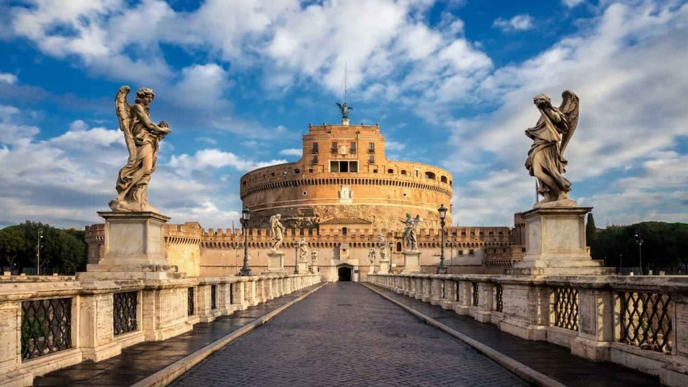 The Colosseum with statues on either side and a cobblestone pathway leading to it. 3