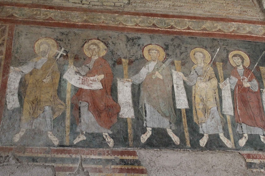 A fresco with religious figures, some holding crosses and others with staffs, on a wall with a decorative border. 2
