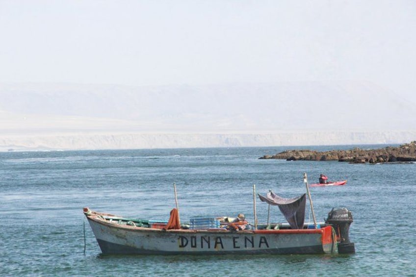 A boat named 'DUNA ENA' on calm water, a rocky shore in the background, and a person in a red kayak. 4