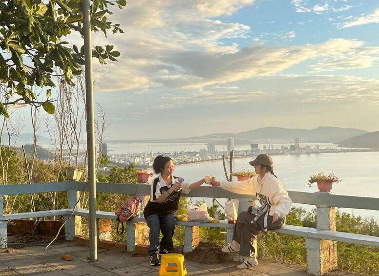 Two people sitting on a bench overlooking a cityscape with a river and mountains in the background. 3