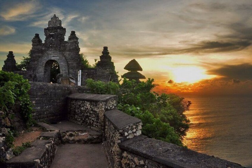 A stone structure with an archway, surrounded by greenery, overlooking a body of water at sunset. 5
