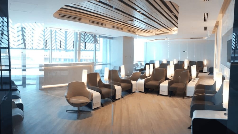 A modern waiting area with chairs and tables, large windows, and a wooden ceiling. 2