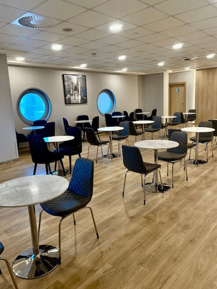 A modern indoor dining area with round tables and chairs, wooden flooring, and circular windows. 4