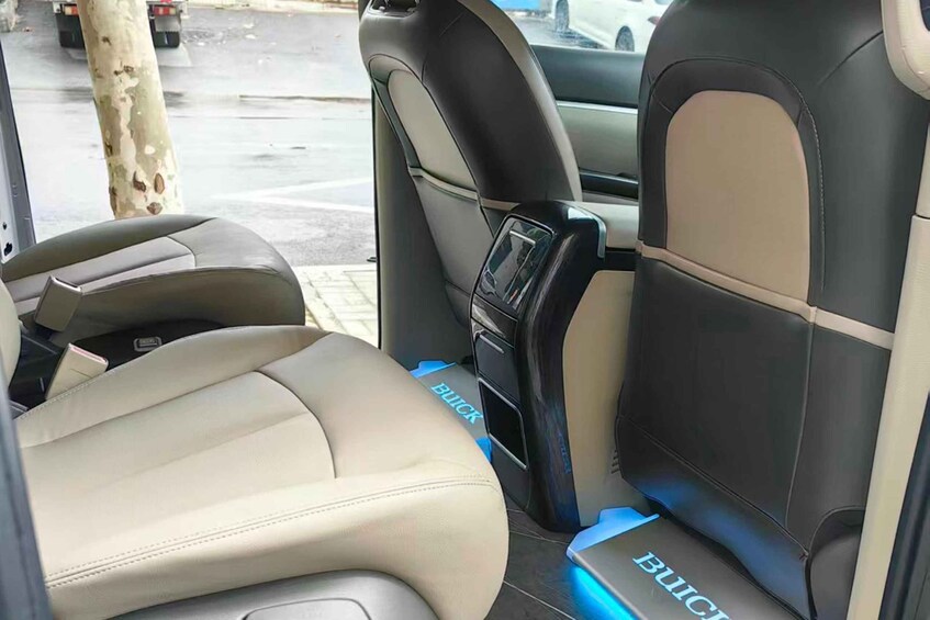 The interior of a vehicle with beige and black leather seats, a visible door handle, and a logo on the seat. 3