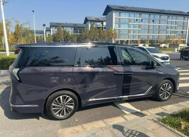 A dark-colored minivan parked on a city street with modern buildings in the background. 2