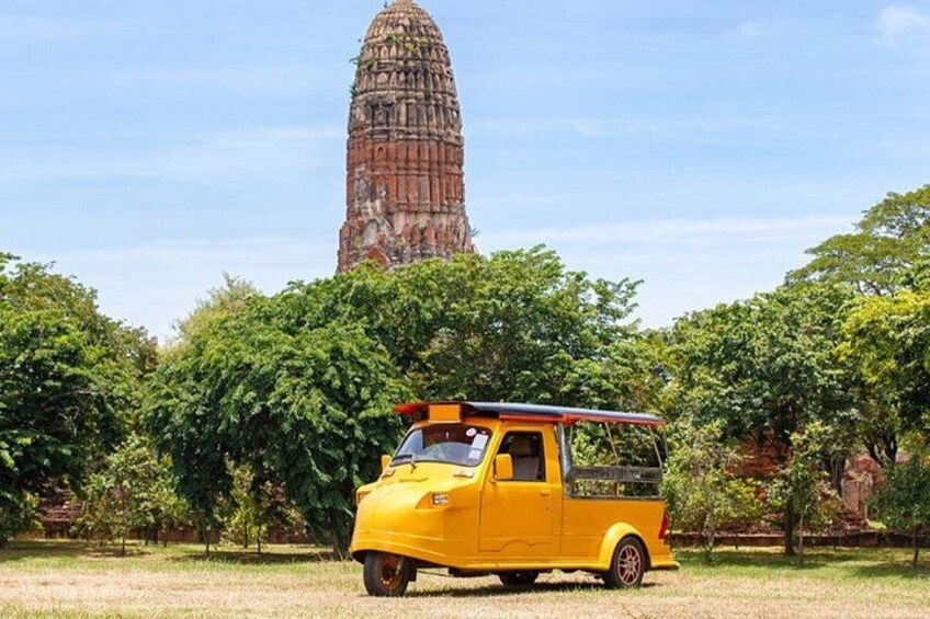 A yellow pickup truck parked in a grassy area with a large, ancient temple in the background. 1