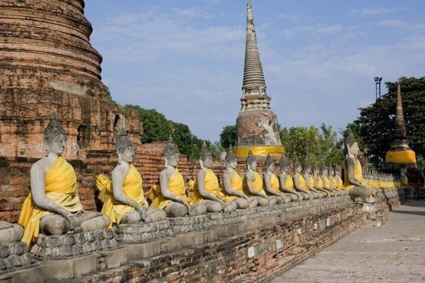Una hilera de estatuas de Buda sentadas, vestidas con túnicas amarillas, una gran estupa y una estructura de ladrillo. 5