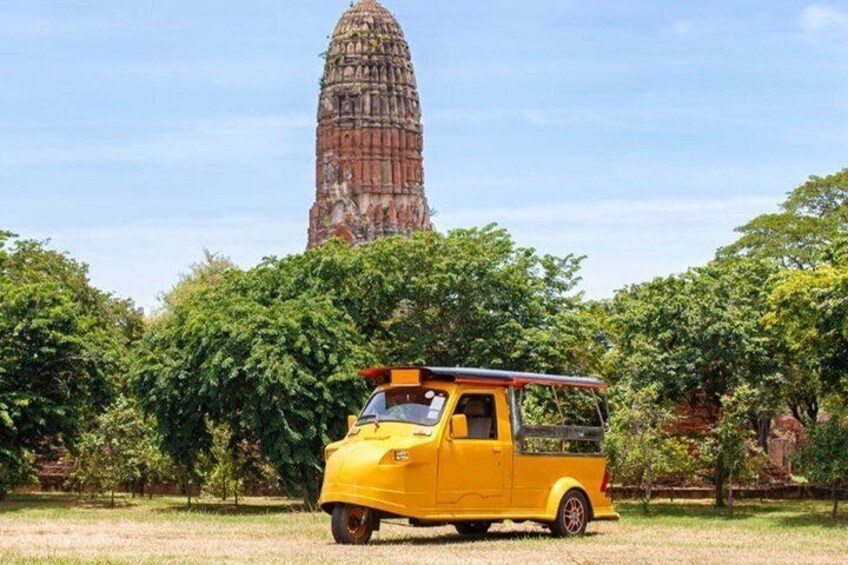 Un vehículo amarillo estacionado en un área con césped, con un templo antiguo y grande al fondo. 1