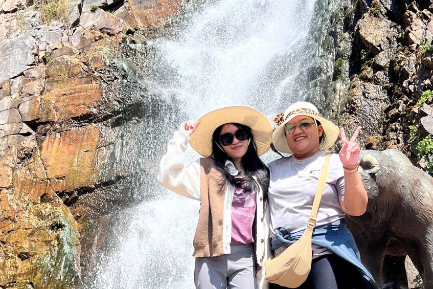 Two people posing in front of a waterfall with a rocky background. 3