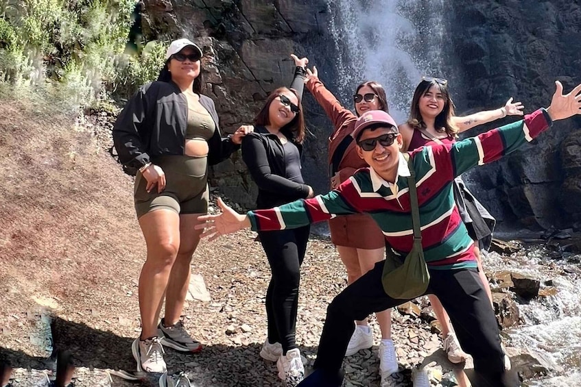 A group of people posing in front of a rocky cliff with a waterfall. 5