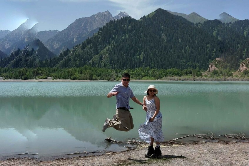 A couple jumping by a calm lake with mountains in the background. 4