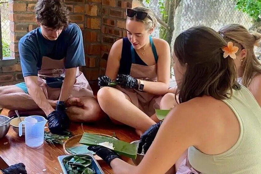 Un groupe de personnes est assis par terre, occupé à préparer un plat à l’aide de divers ingrédients et ustensiles disposés sur une table en bois. 5