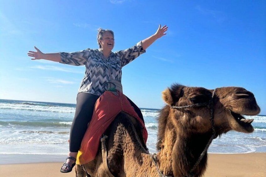 A person riding a camel on a beach with the ocean in the background. 5
