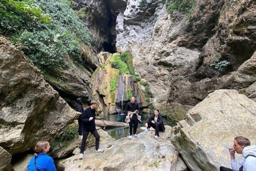 A group of people standing on rocks near a waterfall in a rocky canyon. 5