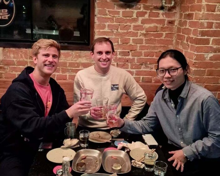 Three people sitting at a table with drinks and plates, in a brick-walled room. 1