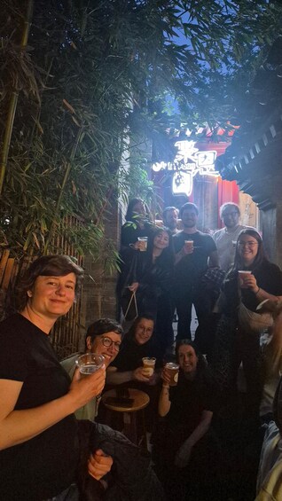 A group of people outdoors at night, holding drinks, with a building and trees in the background. 3