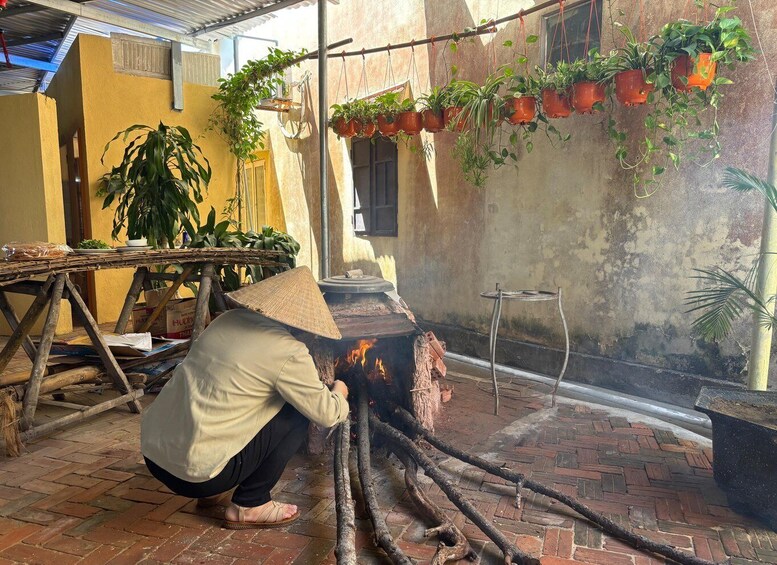 A person cooking over an open fire in a courtyard with hanging plants and a brick floor. 2