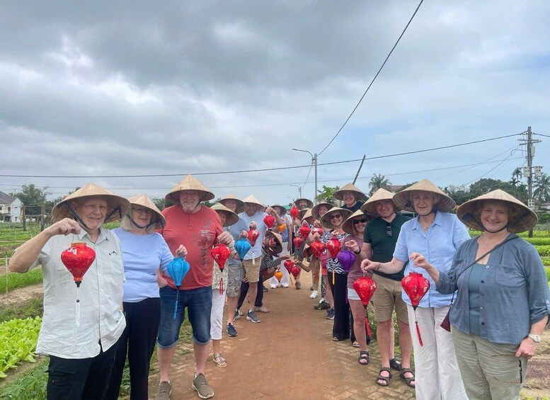 A group of people in traditional conical hats holding red and blue lanterns, walking on a rural path. 5