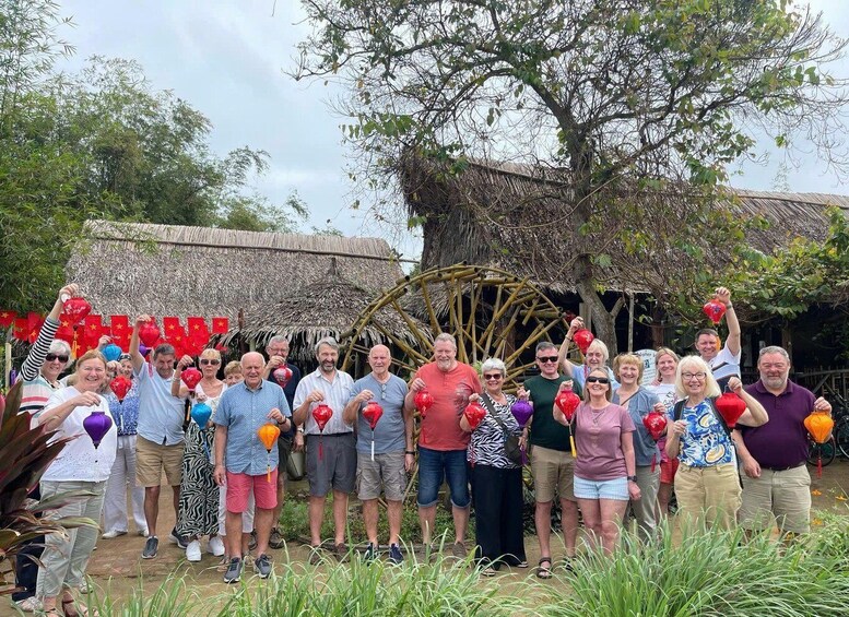 A group of people outdoors with a traditional thatched-roof structure in the background. 1