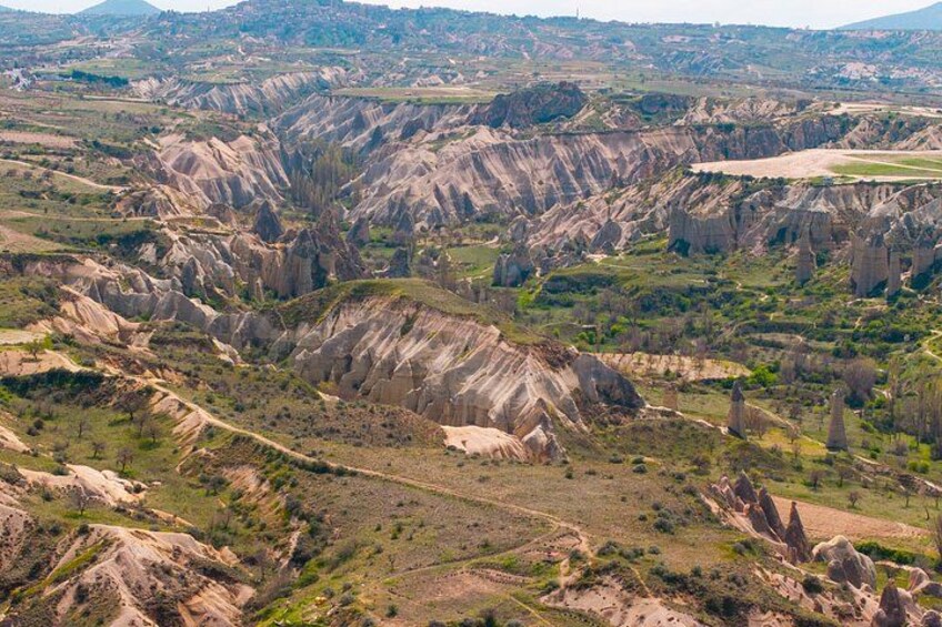 A rugged landscape with eroded hills and valleys, sparse vegetation, and a distant town. 5