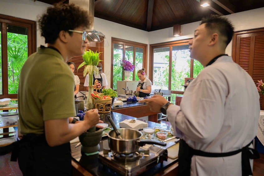 Eine Restaurantküche mit einem Koch, der Speisen zubereitet, einem Buffet mit verschiedenen Gerichten und einem Fenster mit Grünpflanzen draußen. 2