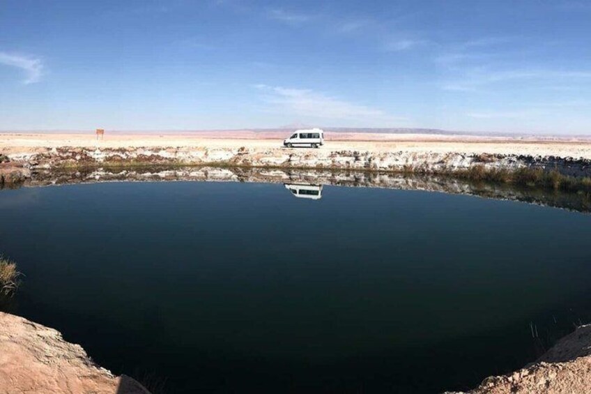 A white vehicle parked by a calm body of water with a desert landscape in the background. 3