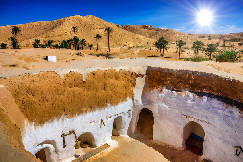 A desert landscape with palm trees, a mountain, and an ancient cave with arches. 4
