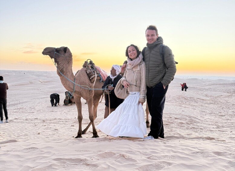 A camel with riders in a desert landscape at sunset. 1