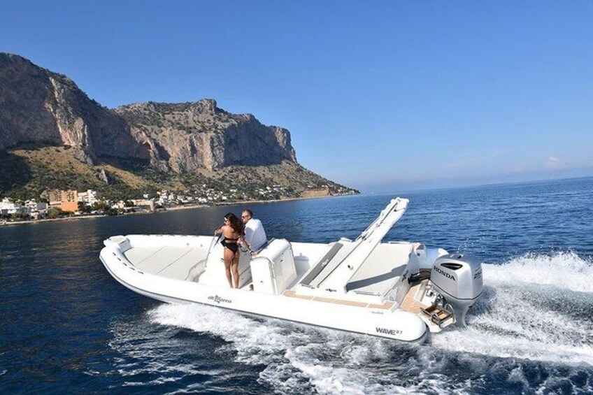 Een witte motorboot met twee personen aan boord, die door het water vaart langs een rotsachtige kustlijn met kliffen op de achtergrond. 2