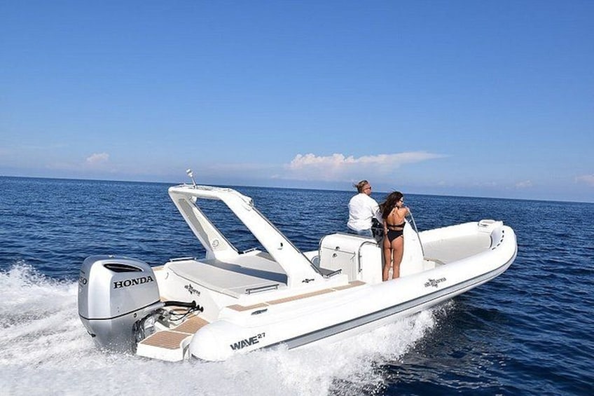 Een witte motorboot met een Honda buitenboordmotor, twee personen aan boord en de oceaan op de achtergrond. 1