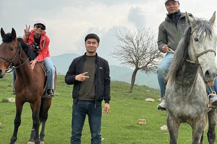 Drie mensen met paarden in een grasveld, met bergen op de achtergrond. 4