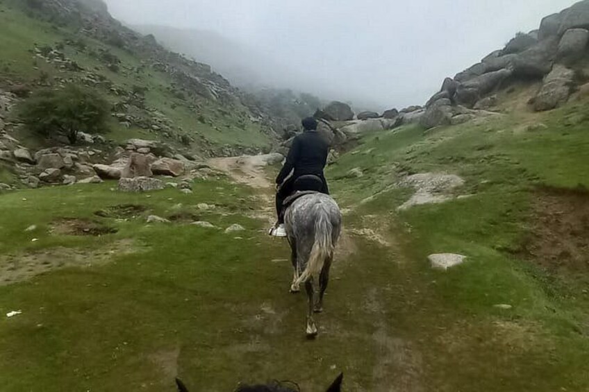 Een persoon te paard op een smal pad, omringd door rotsachtig terrein en schaarse begroeiing. 5