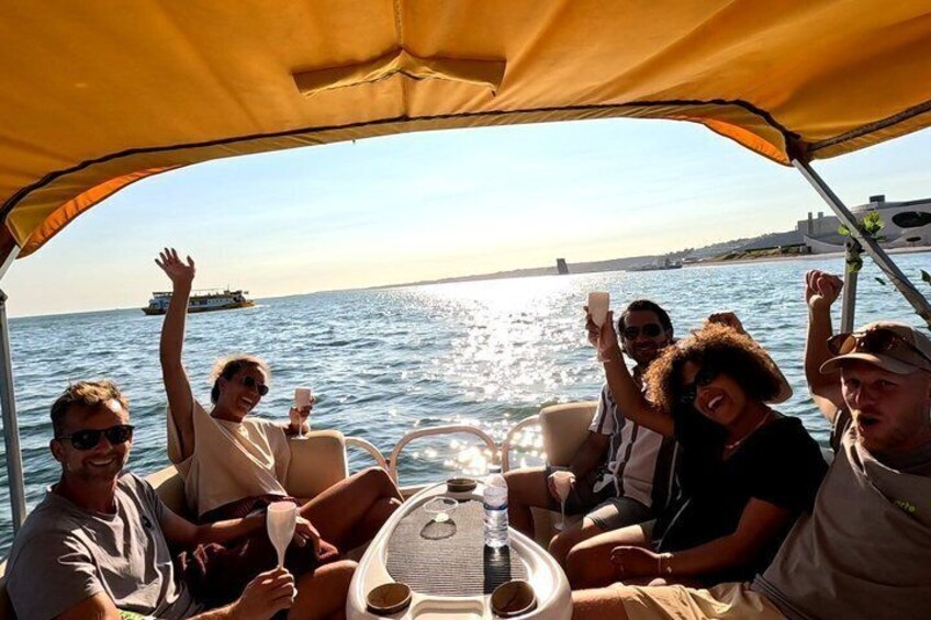 A group of people on a boat with a table, enjoying the view of the sea and a distant ship. 3