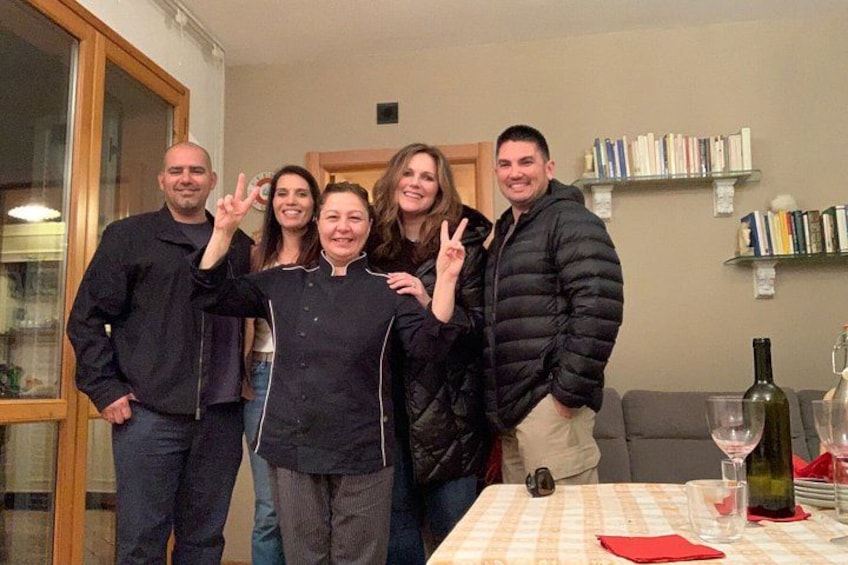 A group of people posing for a photo in a room with a table, bookshelves, and a bottle of wine. 3