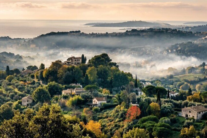 Un village côtier où les maisons sont nichées au milieu des arbres, avec une mer brumeuse et des collines lointaines. 5