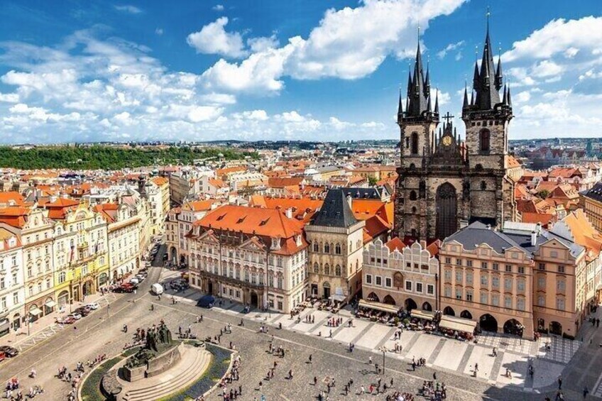 A historic city square with a prominent church tower, surrounded by traditional buildings with red roofs. 5