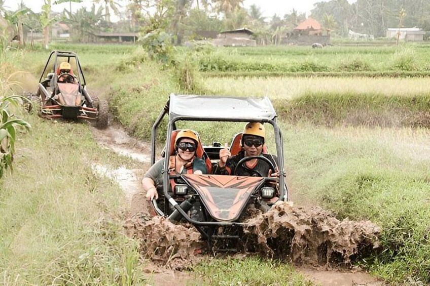 Twee terreinwagens rijden over een modderige weg in een landelijke omgeving, met velden en bomen op de achtergrond. 2