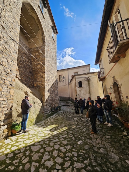 A cobblestone street with stone buildings, a man taking a photo, and people standing and walking. 3