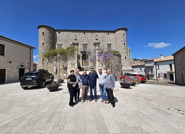 A group of people standing in front of a historic stone building with a tower. 2