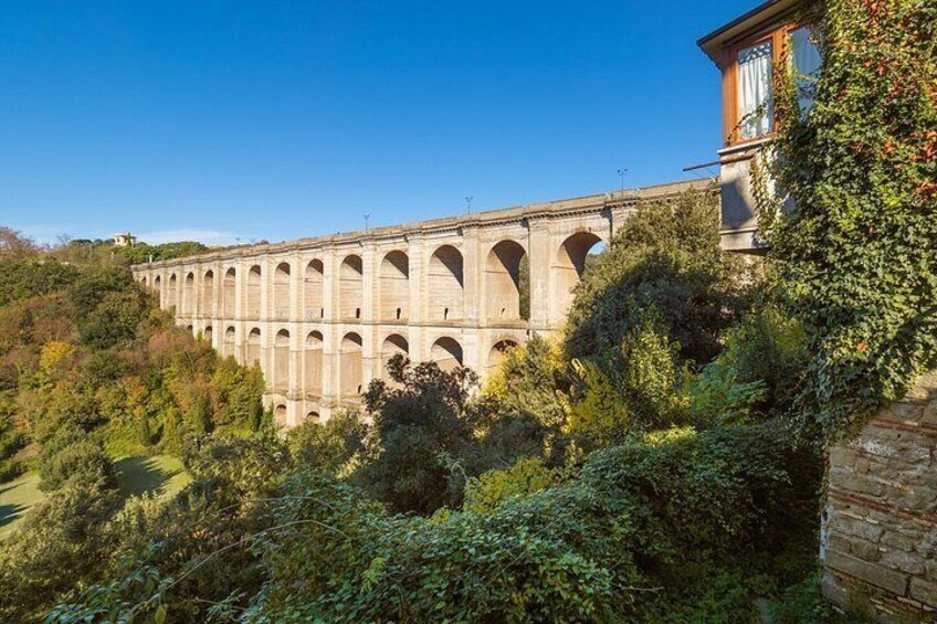 Un viaduc en pierre, doté de nombreuses arches, entouré d’une végétation luxuriante et surplombé d’un ciel bleu clair. 2