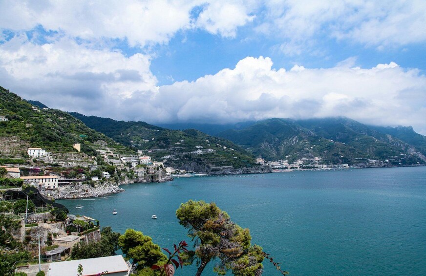 A coastal town with buildings on a hillside, a calm sea, and mountains in the background. 2