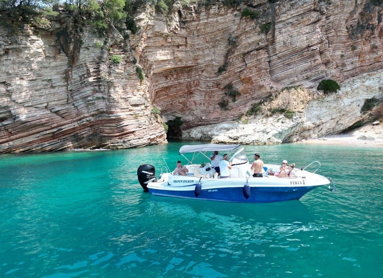 A boat named QUICKSILVER 80 with passengers on a turquoise sea near rocky cliffs. 1