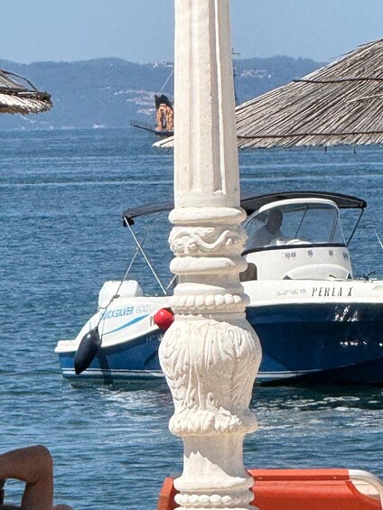 A boat named 'PERLA' docked at a marina with a clear view of the sea and distant mountains. 5