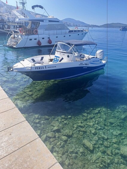 A boat named 'PERLA X' docked at a marina with clear water and rocky bottom visible. 4