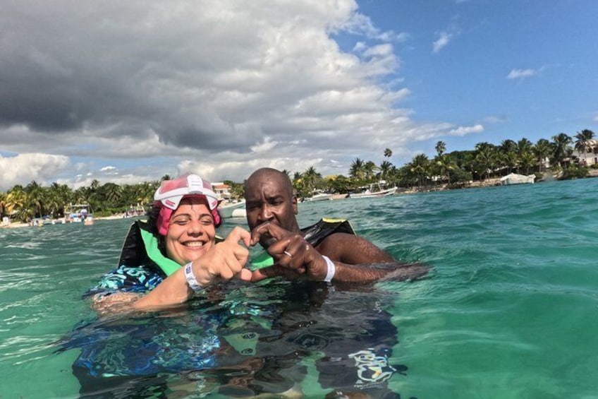 Two people snorkeling in clear turquoise water with a beach and palm trees in the background. 2